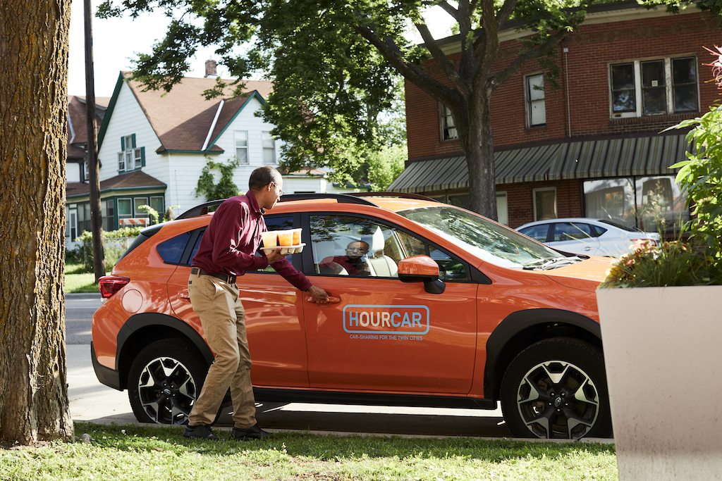 Person walking up to a car with an "HOURCAR" sticker on the side of it