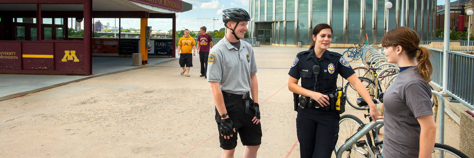 A student talking with a UMPD officer and security guard near a bike rack.